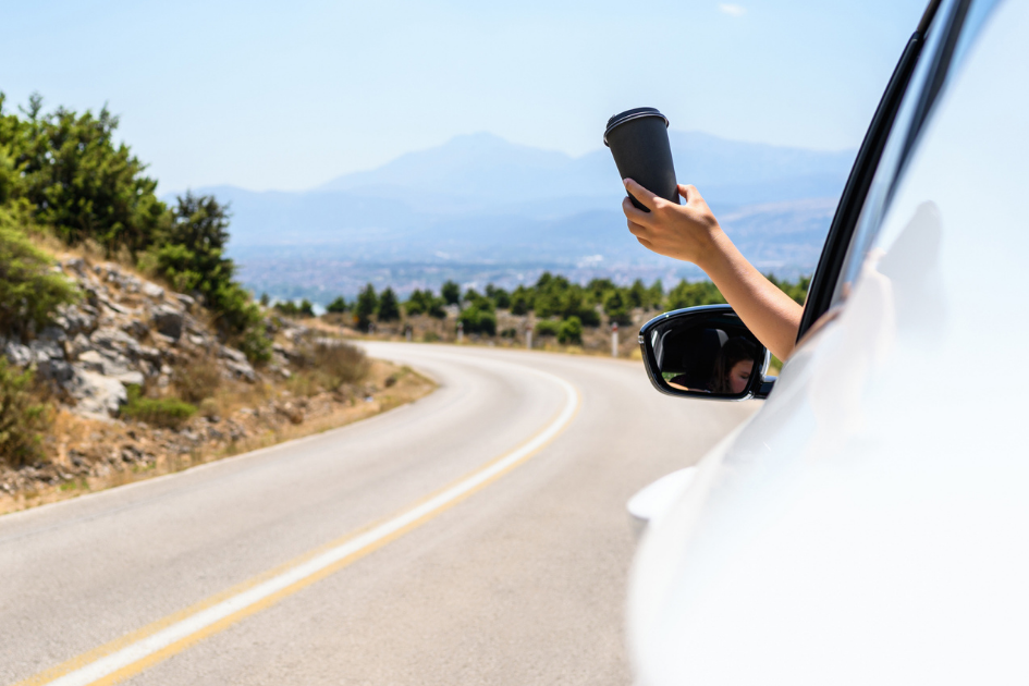 Image of person's arm sticking out of a car window holding a cup of coffee